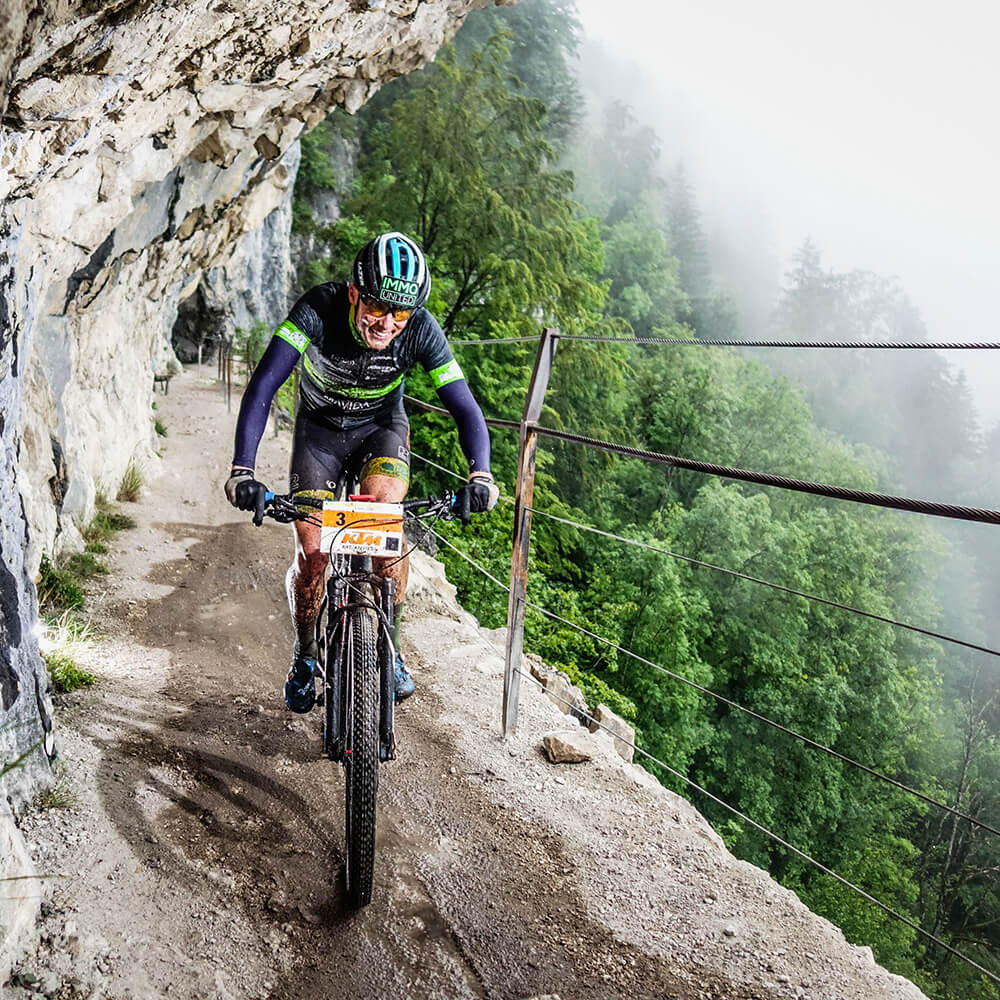 Lukas Kaufmann auf dem Rad auf einem schmalen Bergweg an einer Felswand - Copyright Sportograf.com